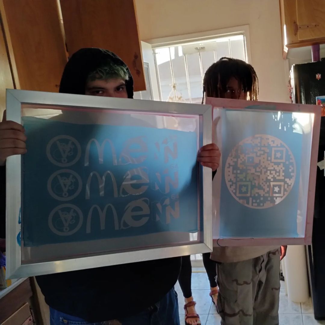 Two people holding screen printing frames with circular text design.