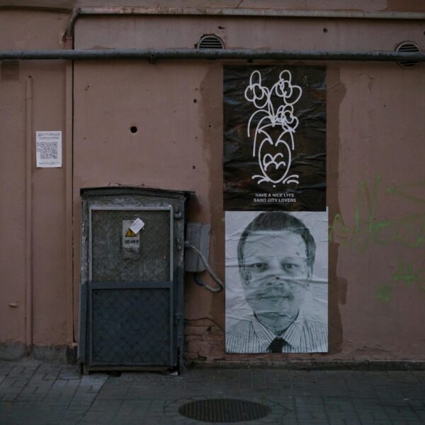 A wall with posters, including a man's portrait and a drawing of flowers.