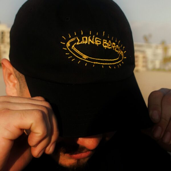 Person wearing a black Long Beach cap, adjusting it with both hands.