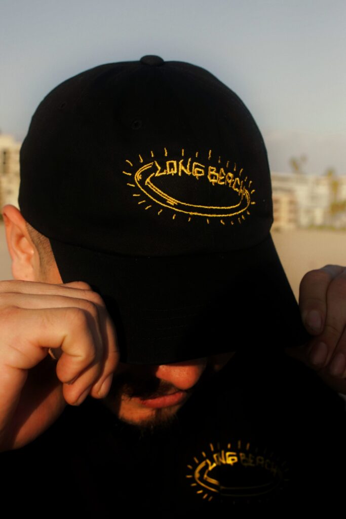 Person wearing a black Long Beach cap, adjusting it with both hands.