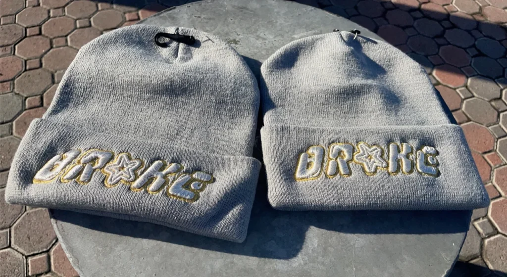 Two gray beanies with embroidered names on a surface.