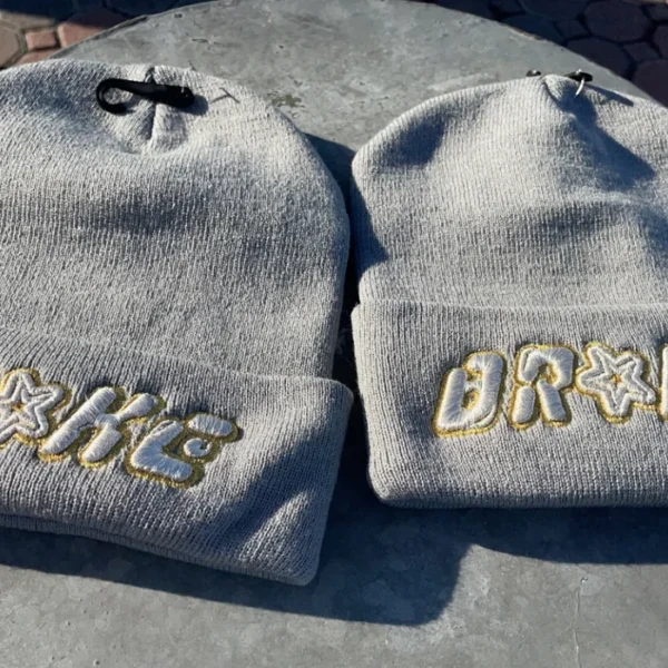 Two gray beanies with embroidered names on a surface.