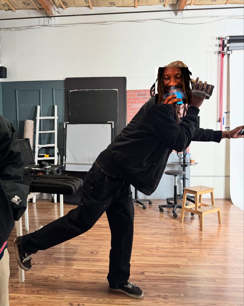 A person in black dancing joyfully in a studio.