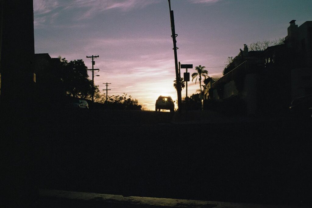 Silhouette of a car against a sunset sky with palm trees.