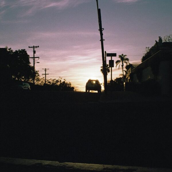 Silhouette of a car against a sunset sky with palm trees.