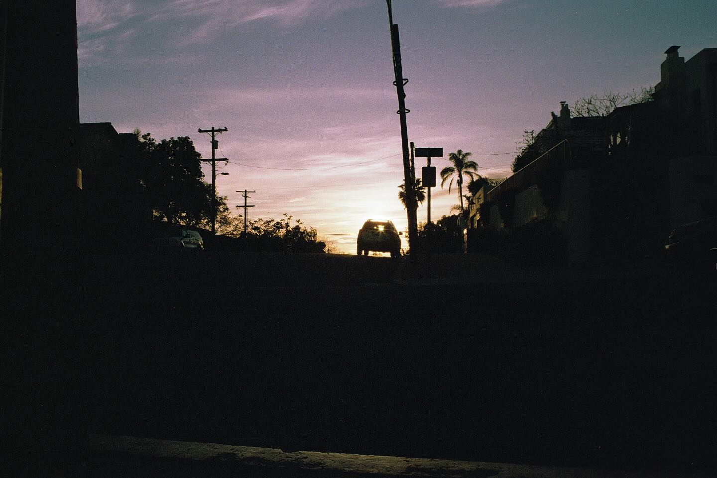 Silhouette of a car against a sunset sky with palm trees.