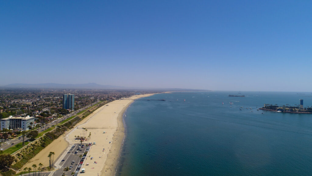 Aerial view of a long sandy beach meeting a calm blue ocean under a clear sky.