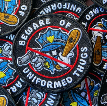 Patch with 'Beware of Uniformed Thugs' featuring a police officer illustration.