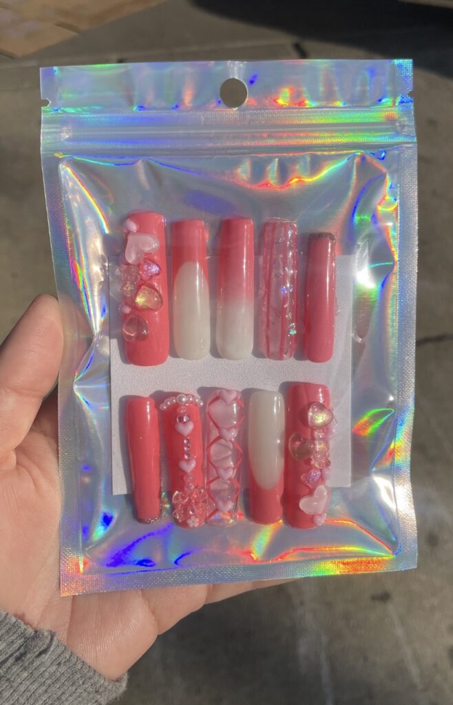 Set of pink and red decorated press-on nails in holographic packaging.